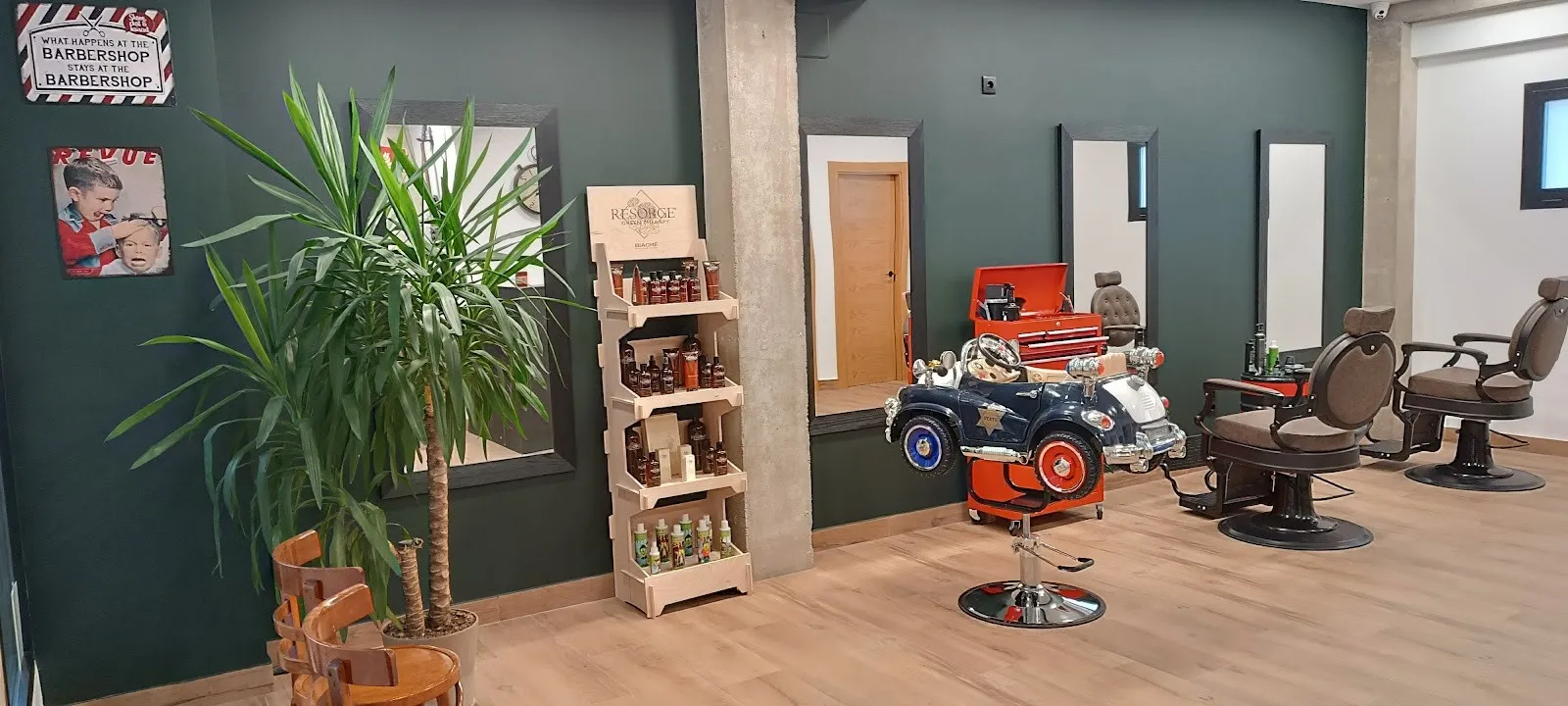Interior de la barbería con los sillones, el coche patrulla infantil y la planta